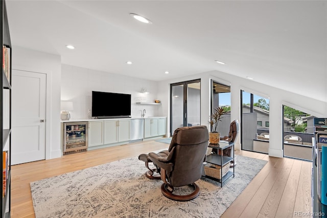 living room featuring lofted ceiling, indoor bar, beverage cooler, and light wood-type flooring