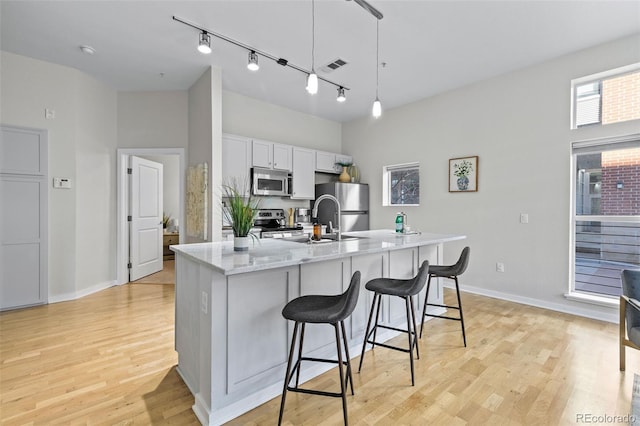 kitchen with light stone counters, stainless steel appliances, decorative light fixtures, light hardwood / wood-style floors, and white cabinetry