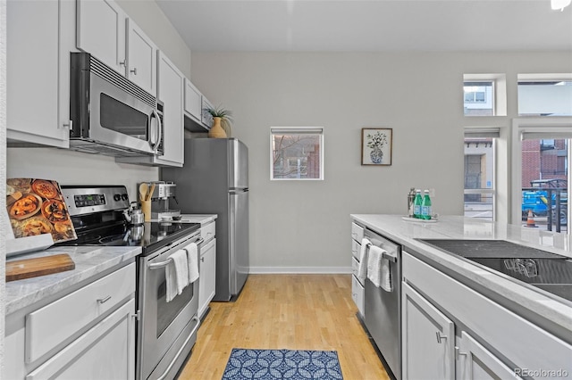 kitchen with light stone countertops, white cabinetry, stainless steel appliances, and light wood-type flooring