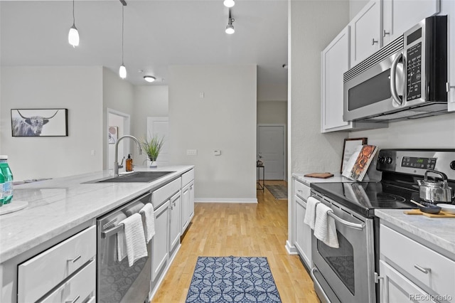 kitchen with white cabinetry, sink, light stone countertops, decorative light fixtures, and appliances with stainless steel finishes