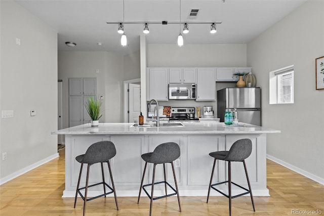 kitchen featuring white cabinets, a kitchen bar, stainless steel appliances, and a large island with sink