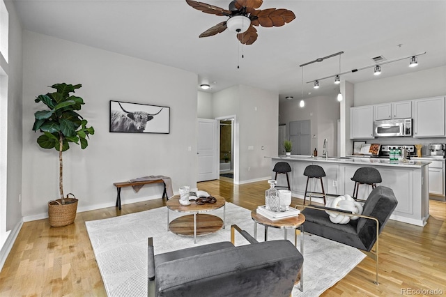 living room with light hardwood / wood-style floors, track lighting, and ceiling fan