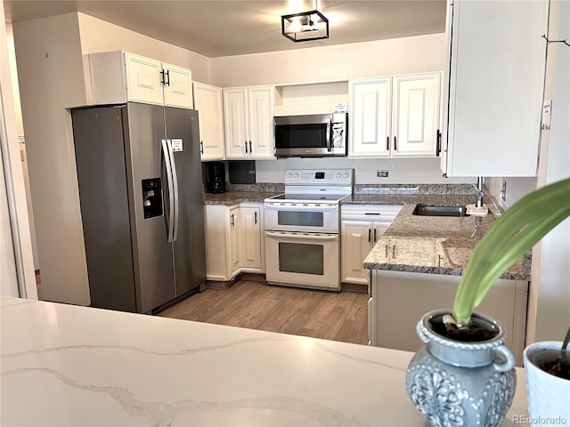 kitchen with stone counters, light wood-style flooring, a sink, white cabinets, and appliances with stainless steel finishes