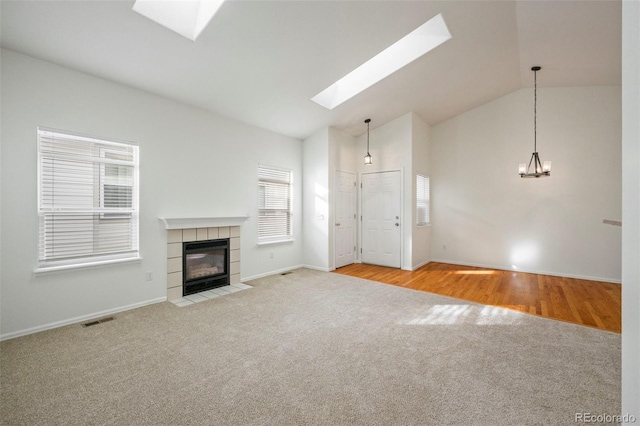 unfurnished living room featuring a tile fireplace, lofted ceiling with skylight, and light hardwood / wood-style floors