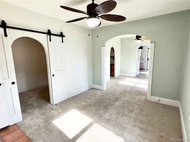 empty room featuring light carpet, a barn door, and ceiling fan