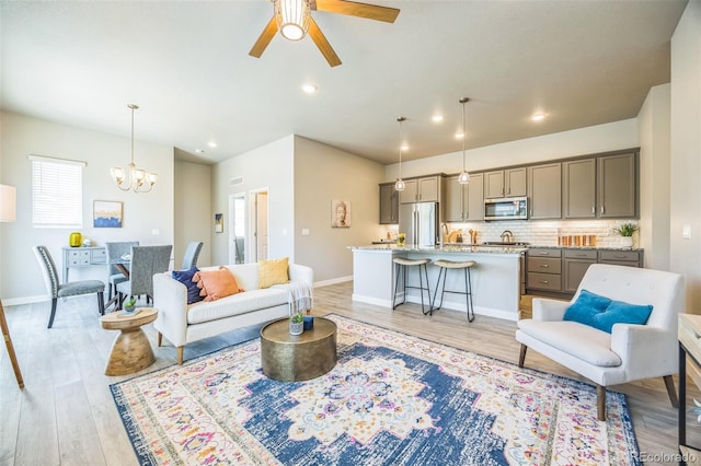 living area with light wood finished floors, a ceiling fan, a chandelier, baseboards, and recessed lighting