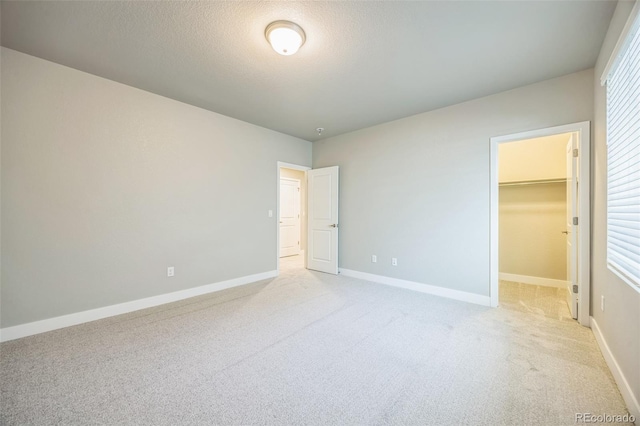unfurnished bedroom featuring light colored carpet, a spacious closet, baseboards, a closet, and a textured ceiling