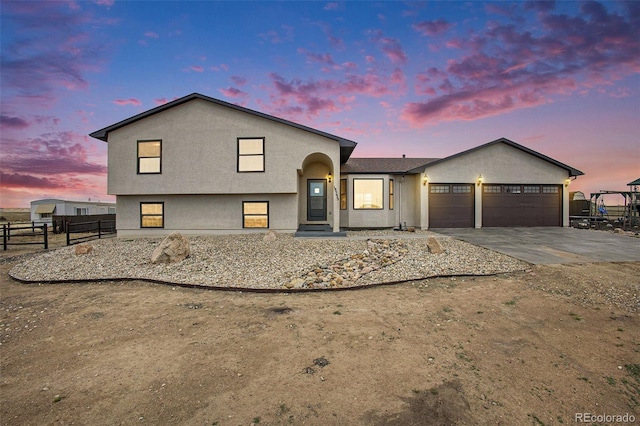 tri-level home with concrete driveway, stucco siding, fence, and a garage
