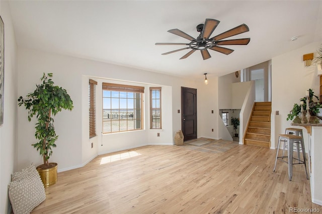 interior space featuring stairs, ceiling fan, baseboards, and light wood-type flooring