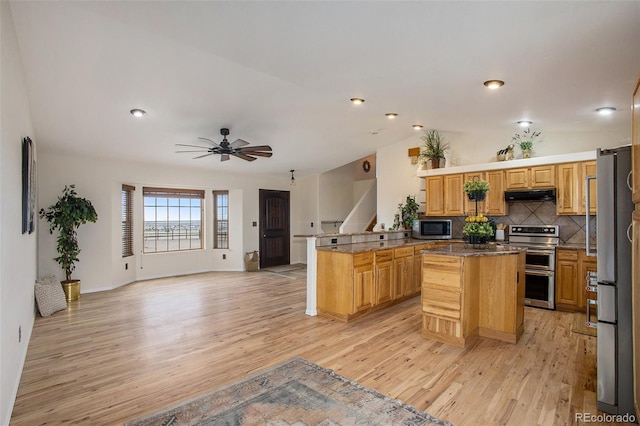 kitchen featuring appliances with stainless steel finishes, light wood-type flooring, under cabinet range hood, and a peninsula