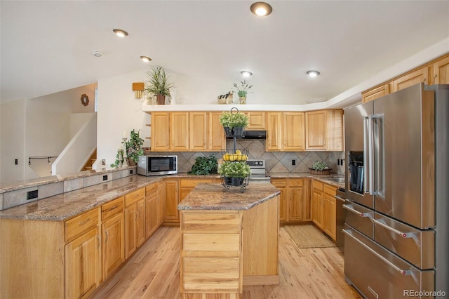 kitchen featuring stainless steel appliances, tasteful backsplash, light wood finished floors, and a peninsula