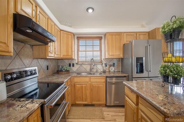 kitchen featuring appliances with stainless steel finishes, a sink, light wood-style floors, stone countertops, and under cabinet range hood