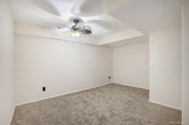 empty room with carpet floors, ceiling fan, baseboards, and a raised ceiling