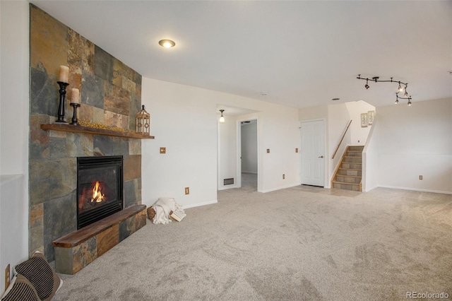 unfurnished living room featuring baseboards, carpet flooring, stairs, and a stone fireplace