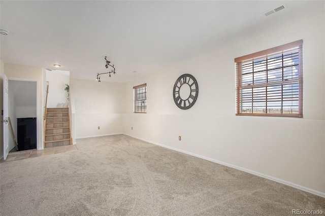 unfurnished living room featuring track lighting, light carpet, stairs, baseboards, and visible vents