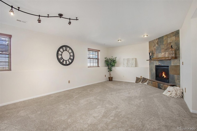 unfurnished living room featuring visible vents, a fireplace, track lighting, baseboards, and carpet flooring