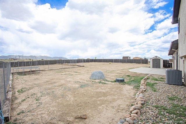 view of yard featuring a fenced backyard, cooling unit, a shed, and a trampoline