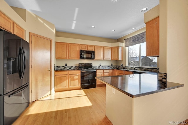 kitchen with kitchen peninsula, sink, light wood-type flooring, dark stone countertops, and black appliances