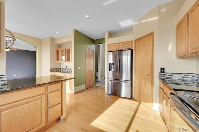 kitchen featuring light brown cabinets, tasteful backsplash, dark stone countertops, and appliances with stainless steel finishes