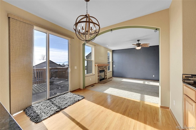 unfurnished living room with ceiling fan with notable chandelier, light hardwood / wood-style flooring, and a fireplace