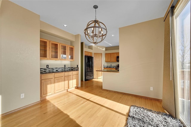 kitchen featuring black fridge, light hardwood / wood-style flooring, hanging light fixtures, tasteful backsplash, and a chandelier