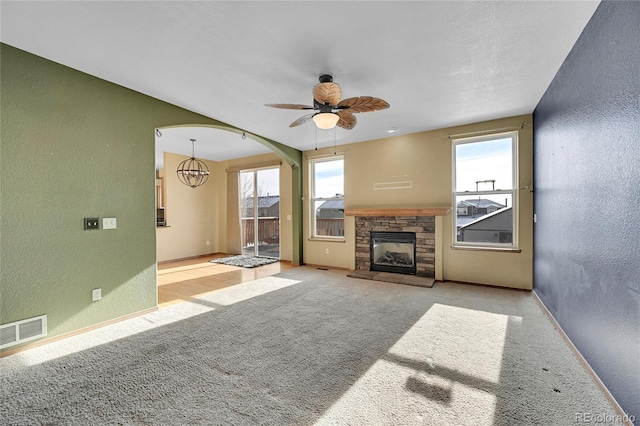 unfurnished living room with a fireplace, ceiling fan with notable chandelier, and light colored carpet