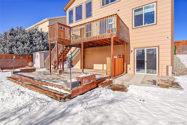 snow covered back of property with a storage shed and a deck