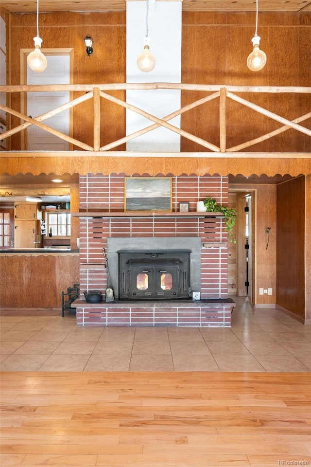 unfurnished living room with tile patterned flooring, a wood stove, wood walls, and a high ceiling