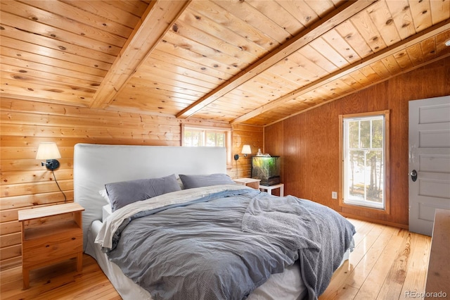 bedroom with vaulted ceiling with beams, wood walls, multiple windows, and light hardwood / wood-style flooring