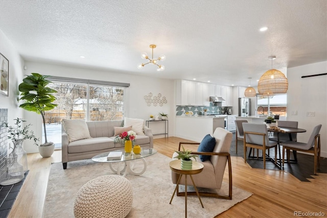 living room featuring light wood finished floors, recessed lighting, an inviting chandelier, a textured ceiling, and baseboards