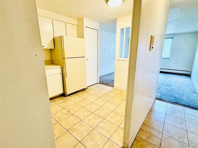 8826 E Florida Ave Unit 102, Denver, CO 80247 - kitchen featuring light tile patterned floors, freestanding refrigerator, white cabinets, a textured ceiling, and baseboard heating