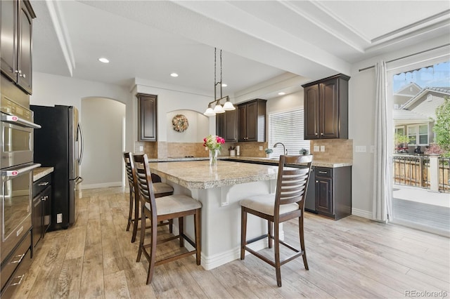 1673 Morningview Ln, Castle Rock, CO 80109 - kitchen featuring stainless steel appliances, arched walkways, dark brown cabinets, a kitchen breakfast bar, and light wood-type flooring