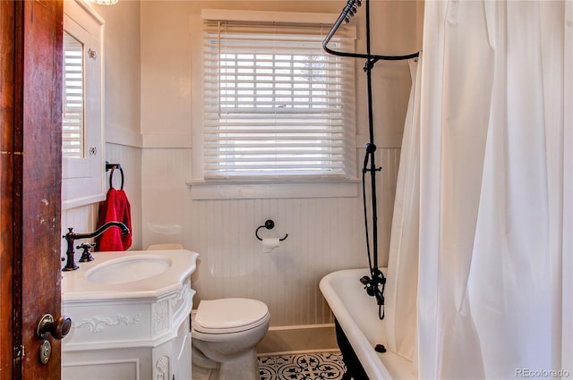 bathroom with toilet, a tub to relax in, wainscoting, and vanity