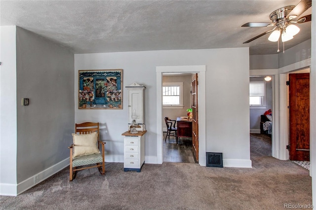 sitting room featuring a textured ceiling, dark carpet, visible vents, and baseboards