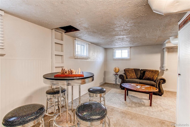 living area with a textured ceiling, a wainscoted wall, and light colored carpet