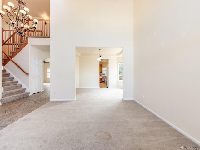 interior space featuring a notable chandelier, a towering ceiling, baseboards, stairs, and carpet