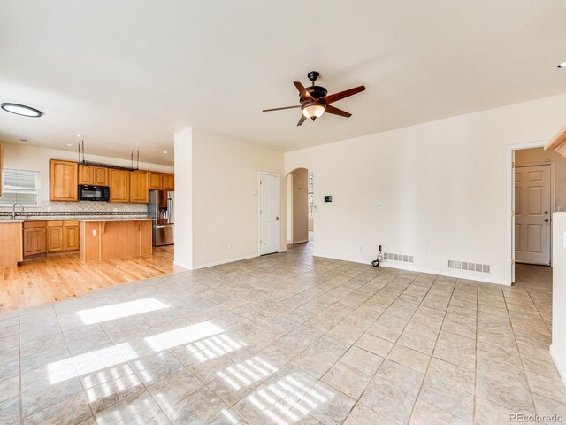 unfurnished living room featuring baseboards, visible vents, arched walkways, ceiling fan, and a sink