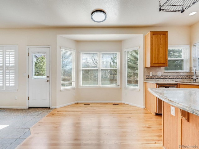 kitchen featuring tasteful backsplash, a sink, light stone countertops, light wood-type flooring, and dishwasher