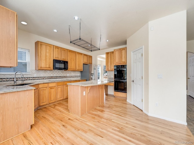 kitchen featuring light stone counters, a sink, a kitchen island, backsplash, and black appliances