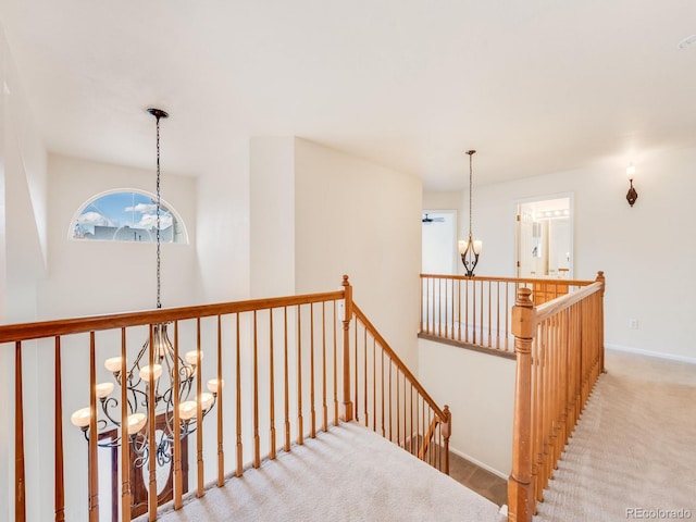 hall featuring baseboards, carpet flooring, a notable chandelier, and an upstairs landing