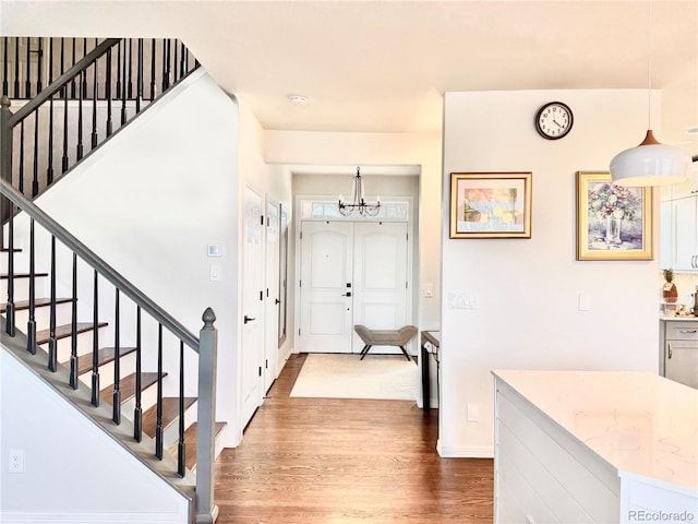 foyer featuring wood finished floors, baseboards, stairway, and an inviting chandelier