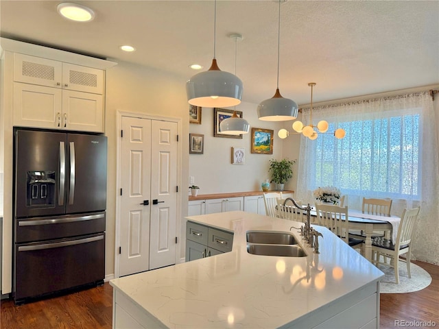 kitchen featuring an island with sink, dark wood-style flooring, fridge with ice dispenser, and a sink