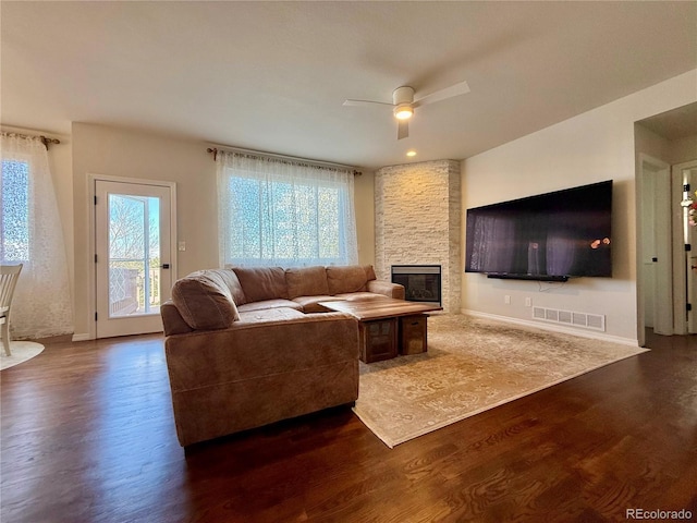 living room featuring a ceiling fan, a fireplace, dark wood-style flooring, and a healthy amount of sunlight