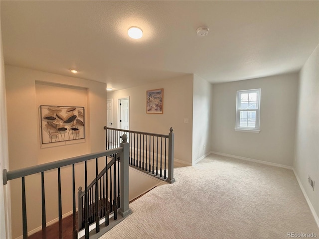 hall with baseboards, carpet floors, and an upstairs landing