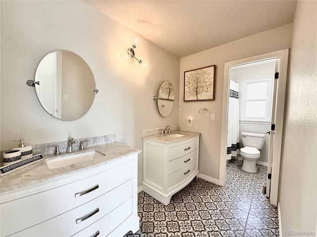 full bath featuring toilet, two vanities, a sink, and baseboards