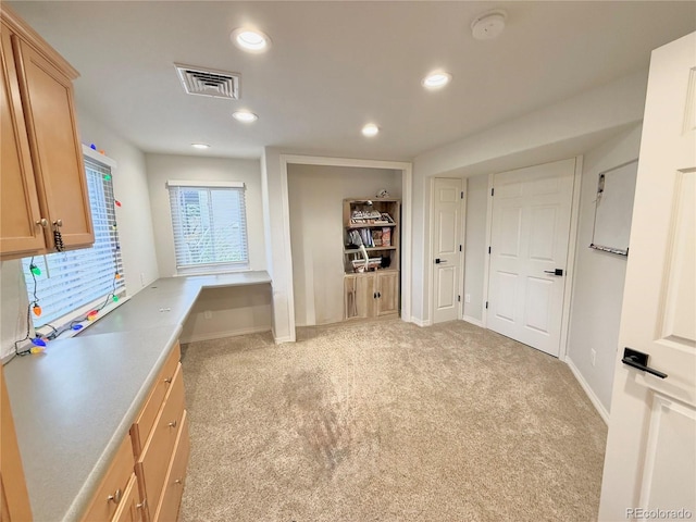 interior space with light colored carpet, visible vents, and built in desk