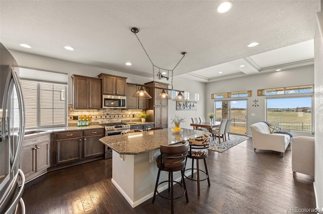 kitchen with dark wood-style floors, appliances with stainless steel finishes, a kitchen breakfast bar, stone counters, and backsplash