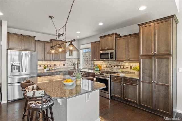 kitchen featuring light stone countertops, stainless steel appliances, dark wood-style flooring, a kitchen island, and decorative backsplash