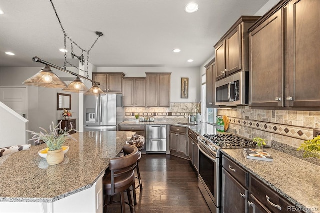 kitchen with appliances with stainless steel finishes, backsplash, dark wood-style flooring, light stone countertops, and a sink