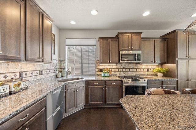 kitchen with light stone counters, dark wood-type flooring, a sink, stainless steel appliances, and backsplash